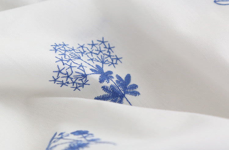 White fabric with a blue botanical pattern, shown in a close-up view with soft folds.